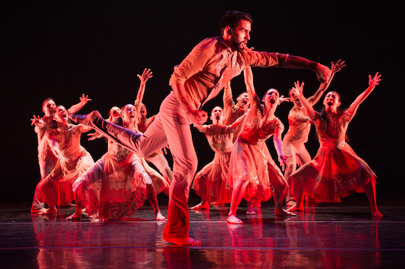 A group of female dancers outstretch their arms with their mouths agape as a male soloist dancers in front of them